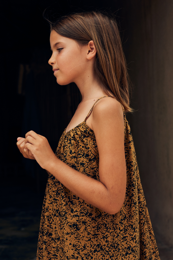 side view of the kids model wearing the cala kids dress in amber color